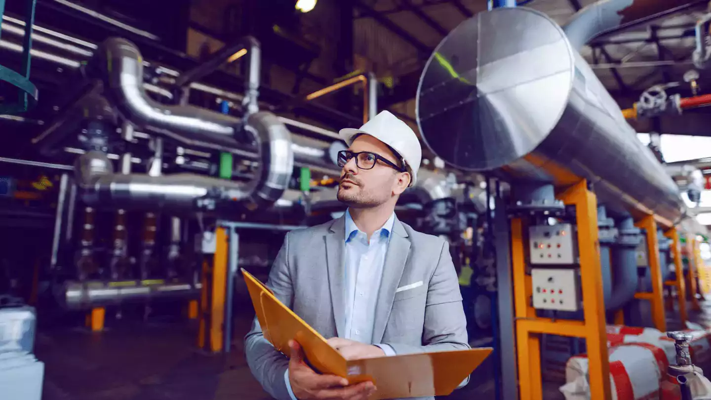 Man with portfolio and hardhat reviewing a plant